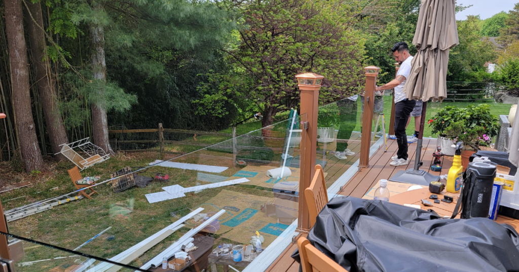 The Glass Guys busy at work installing a glass railing around the perimeter of a deck behind a house.